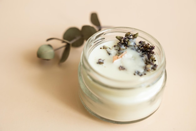 Handmade candle from paraffin and soy wax in glass with wooden wick and dry herbal isolated on pastel beige background Flat lay top view copy space