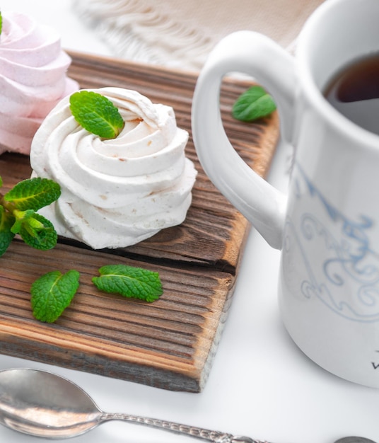 Handmade cream and strawberry marshmallows Adorned with mint leaves Tea in a white cup with a blue ornament On a wooden background Closeup