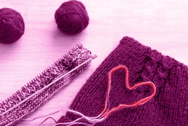 Handmade gifts for the holiday: skeins of purple yarn, knitting needles, finished product, heart made of threads, top view, space for text