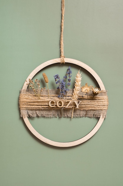 Handmade home decor from a wooden circle and dried flowers with the inscription Cozy