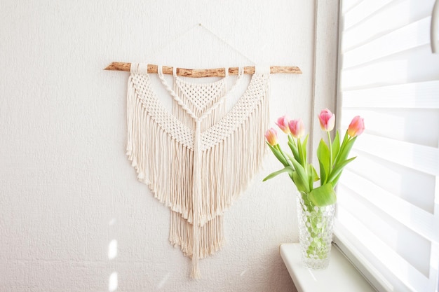 Handmade macrame 100 cotton wall decoration with wooden stick hanging on a white wall