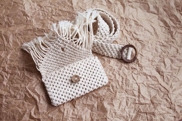 Handmade macrame belt bag on craft paper background ECO friendly natural macrame cotton waist bag Hobby knitting handmade macrame Modern summer concept Copy space