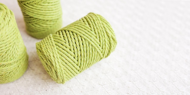 Handmade macrame braiding and cotton threads on textile white background Green cotton macrame cord and rope Good image for macrame and handicrafts banners and advertisement Close up