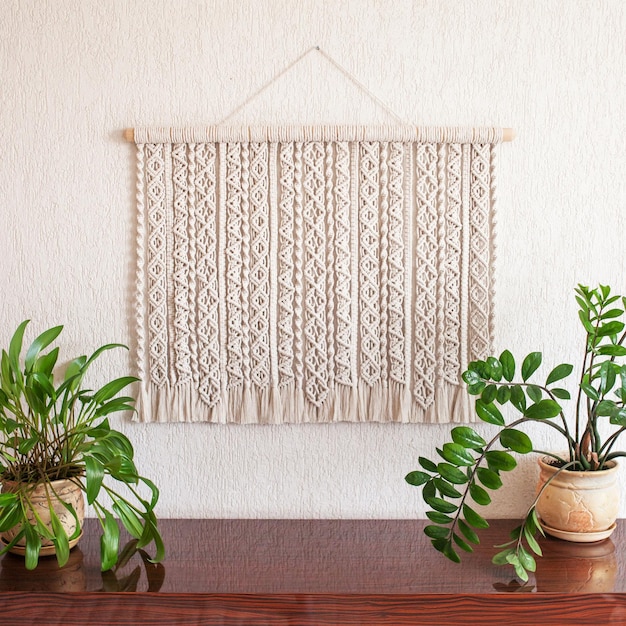 Handmade macrame cotton wall decoration with wooden stick hanging on a white wall