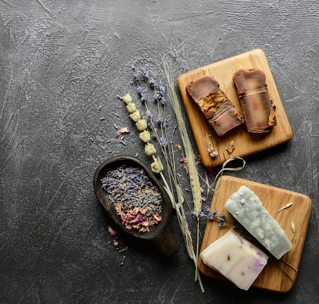 Handmade organic Soap oa a wooden stand with Dried herbs, lavender and rose petals on a black textured background