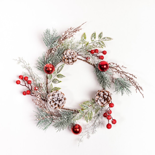 Handmade reusable Christmas wreath made of synthetic tree branches, red berries, cones on white