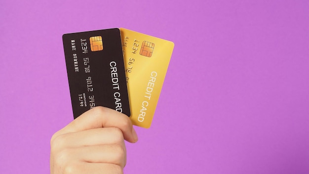 Hands are holding black and gold credit cards on purple background