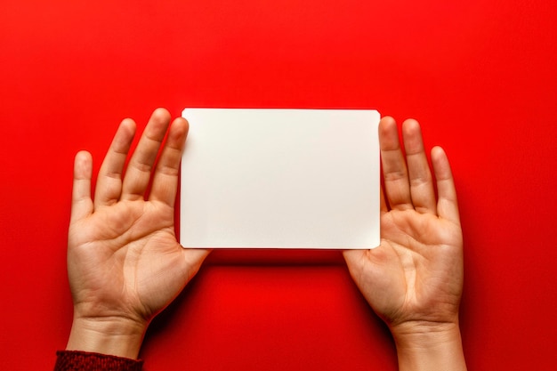 Hands are holding a blank white piece of paper on a red background