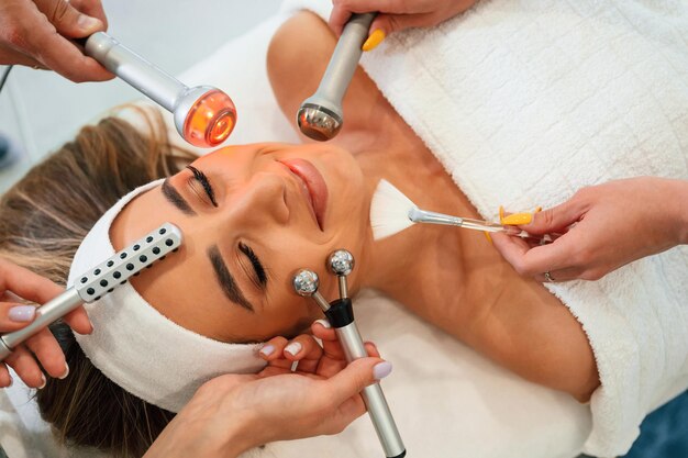 Hands are holding bunch of cosmetitian tools Woman face getting facial care by beautician hands at spa salon