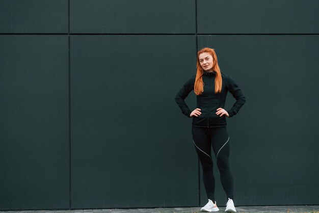 Photo hands are on the waist woman is sportive clothes is outdoors against black building