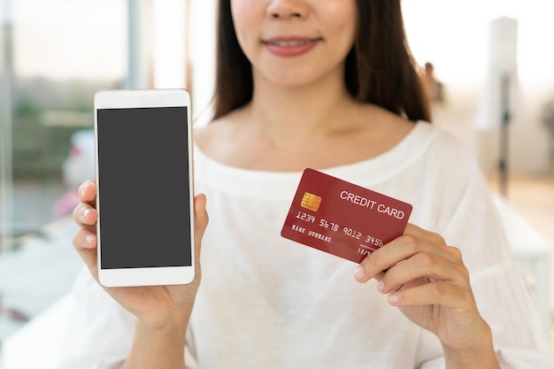 Hands of Asian woman show mobile phone with blank screen for copy space advertisement while holding credit card Close up Technology and lifestyle Cashless society concept