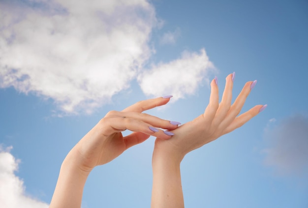 Hands of a beautiful wellgroomed violet lavender nails gel polish on a sky blue background