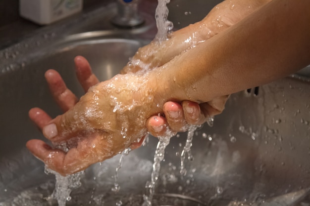  hands being washed under stream of  water from tap