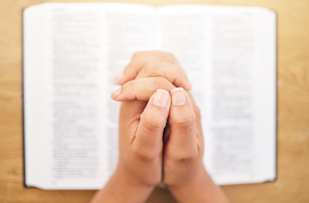 Hands bible and desk for prayer closeup and mindfulness for faith religion or reading in pov Woman praying and study holy book for peace mental health and worship with praise to God in top view