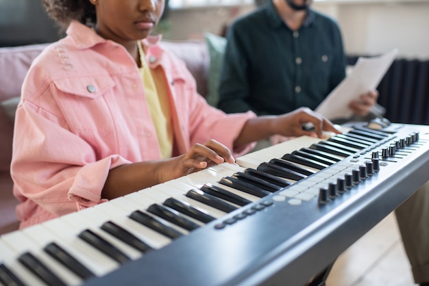 Hands of biracial diligent schoolgirl playing piano keyboard