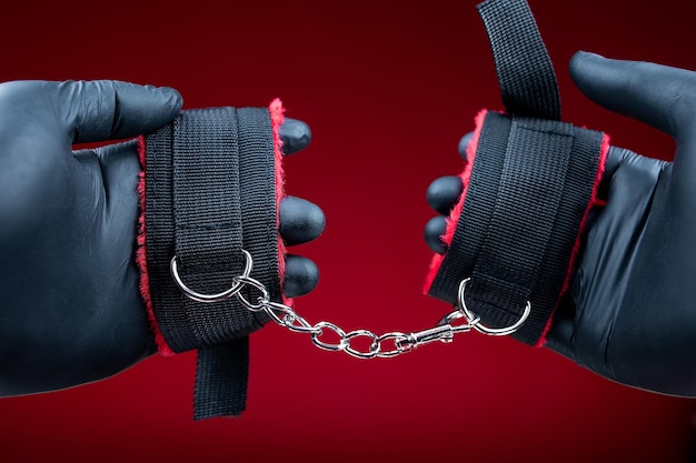 Hands in black gloves holding handcuffs with red belts for bdsm sex games