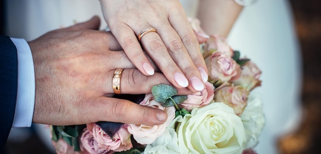 Hands of bride and groom with gold rings on a vintage wedding bouquet, close up. Concept of happy marriage day.