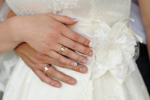 Hands of the bride and groom with rings on a white dress