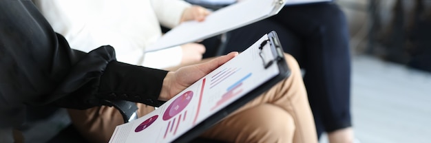 Hands of business employees with documents and charts with financial indicators sitting on chairs