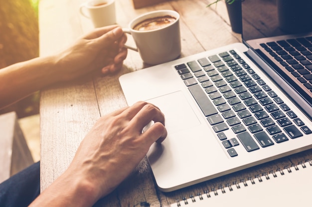 Hands of business man typing on a laptop and holding coffee in coffee shop.