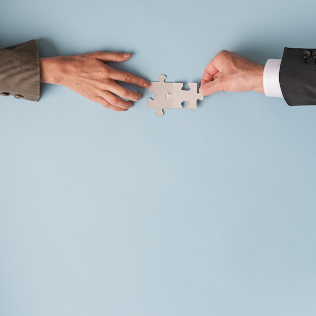 Hands of a businessman and businesswoman joining two blank matching puzzle pieces