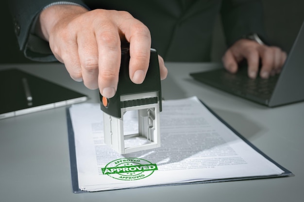 Hands of businessman stamp on paper document to approve business investment contract agreement Closeup Of Person Hand Stamping With Approved Stamp On Document At Desk