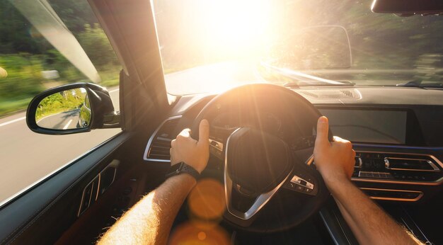 hands of car driver on steering wheel, road trip, driving on forest road with bright sunlight