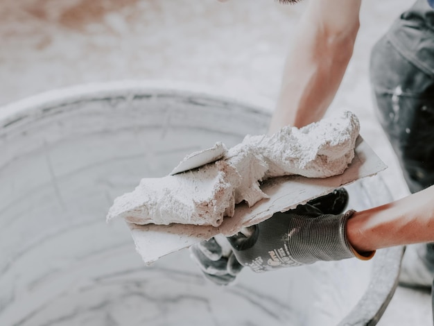 The hands of a Caucasian male plasterer i apply fresh putty with one spatula to another