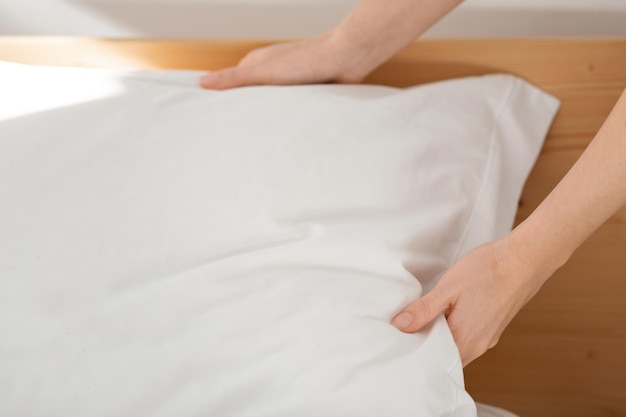 Hands of caucasian millennial female puts soft white pillow on comfortable bed makes bed