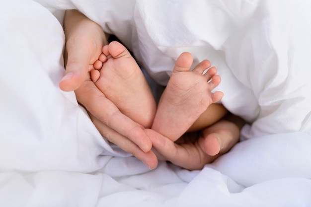 Hands of a Caucasian mom holding the small legs of her baby black African baby.