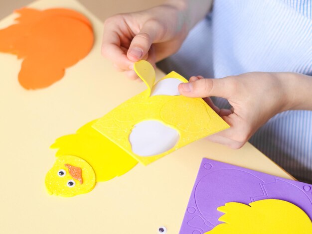 Hands of a caucasian teenage girl peeling off a wing sticker on a yellow chicken felt