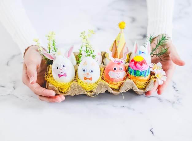 The hands of a caucasian teenager girl hold a cardboard package with Easter decorated eggs