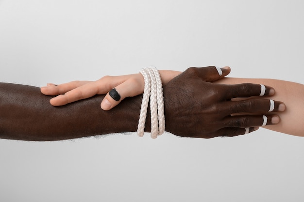 Hands of Caucasian woman and African-American man tied together with rope on light background. Racism concept