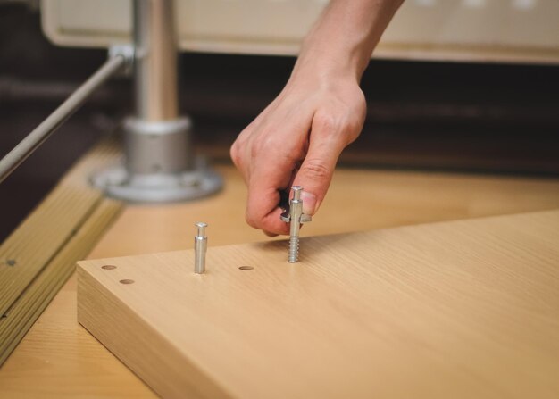 Photo the hands of a caucasian young man with a wrench tighten a bolt on the wooden part of the bed