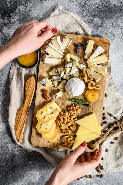 Hands of the chef holding a cheese platter served with nuts and figs. Gray background. Top view