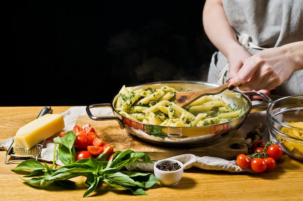 Hands of chef preparing Penne pasta with spinach. 