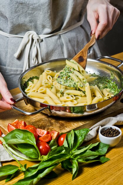 Photo hands of chef preparing penne pasta with spinach. 