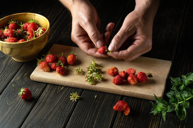 Hands chef sorting through fresh strawberries on the cutting board of the kitchen to prepare a soft drink with mint Cooking diet desserts