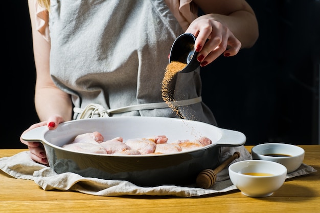 The hands of the chef sprinkles spices raw chicken wings.