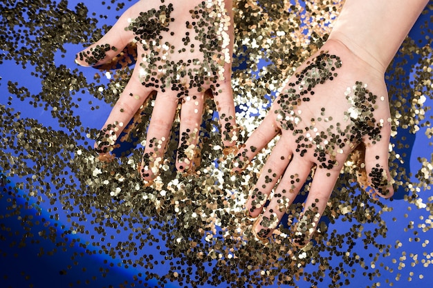 Hands of a child in gold glittering confetti on a blue background, top view. Birthday and holiday .