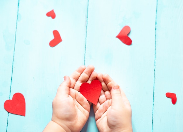 The hands of a child holding a red heart on a blue background