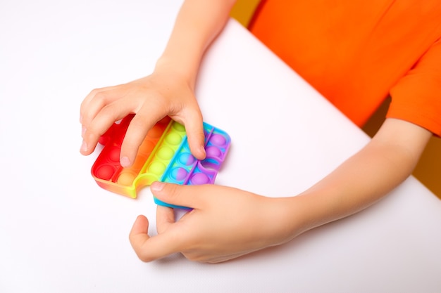 Hands of a child at a white table playing with a silicone anti-stress toy bursts bubbles with his fingers