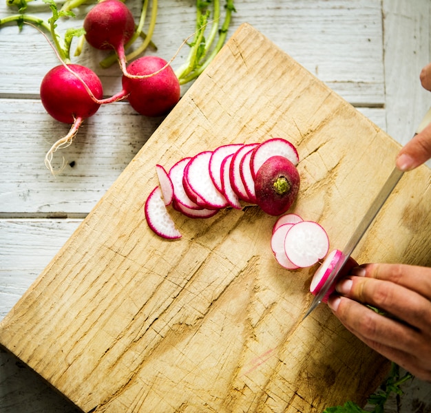 Hands chopping radish on wooden cutting board