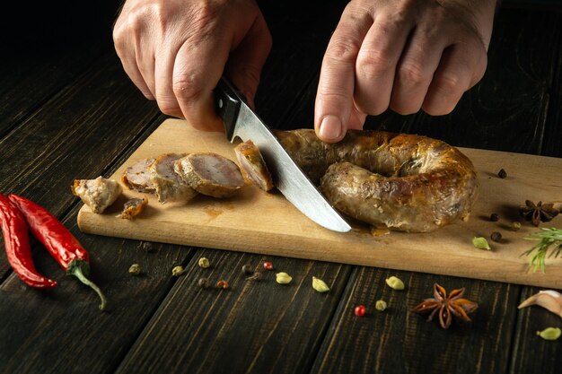 The hands of the cook with a knife cut grilled pork sausage on a cutting kitchen board for a delicious lunch Northern Thailand national dish