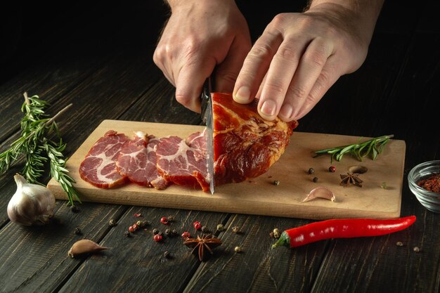 Photo the hands of the cook with a knife cut into small pieces the baked beef on the kitchen cutting board the concept of fast food or making sandwiches on a black background