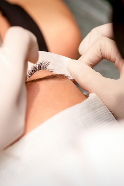 The hands of the cosmetologist are gluing white tape under the eye of the young caucasian woman during the eyelash extension procedure closeup