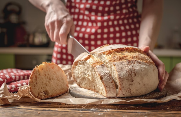 Hands cut with a knife homemade natural fresh bread with a Golden crust on wooden background Baking bakery products