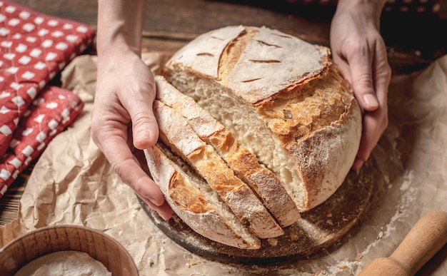 Hands cut with a knife homemade natural fresh bread with a Golden crust on wooden background Baking bakery products