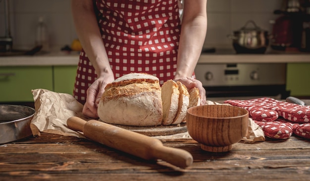 Hands cut with a knife homemade natural fresh bread with a Golden crust on wooden background Baking bakery products