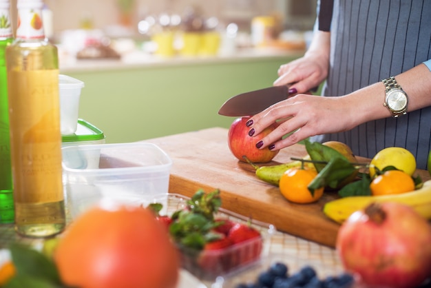 Hands cutting an apple on chopping board. Young woman preparing a fruit salad in her kitchen